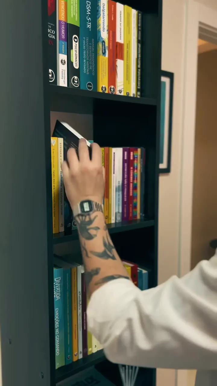 Guilherme pegando um livro na estante do consultório